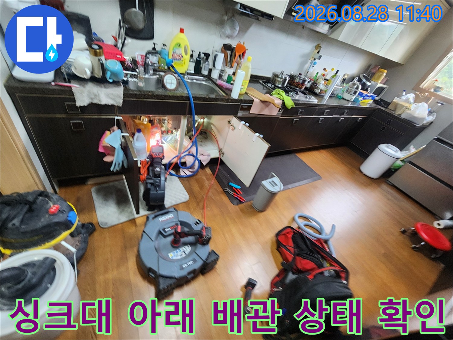 싱크대 밑부분에 배치된 전문 장비와 점검 중인 배관의 모습입니다.