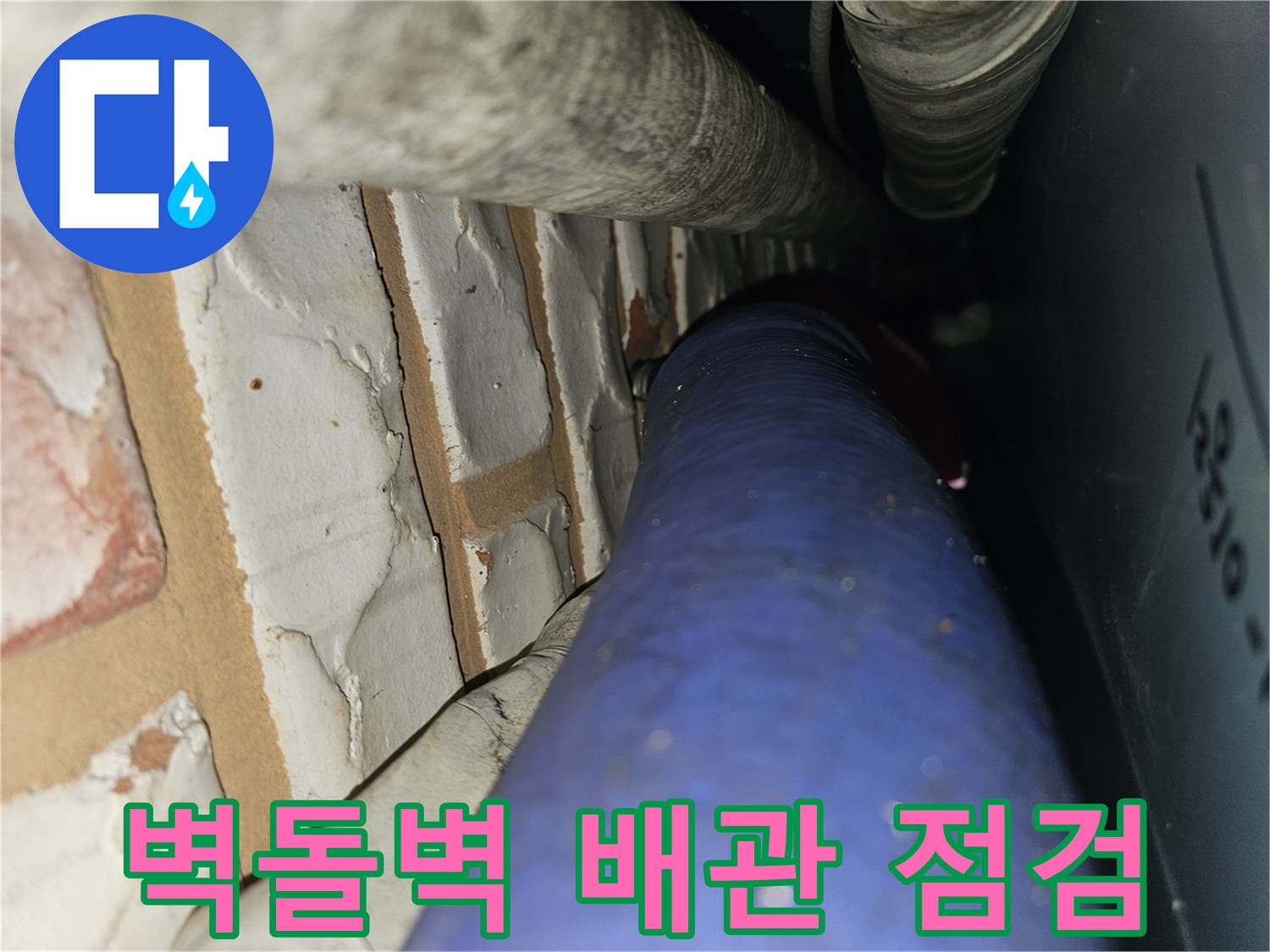 벽돌 구조물 사이로 지나가는 파란색 수도 배관과 보온재 처리된 관의 모습