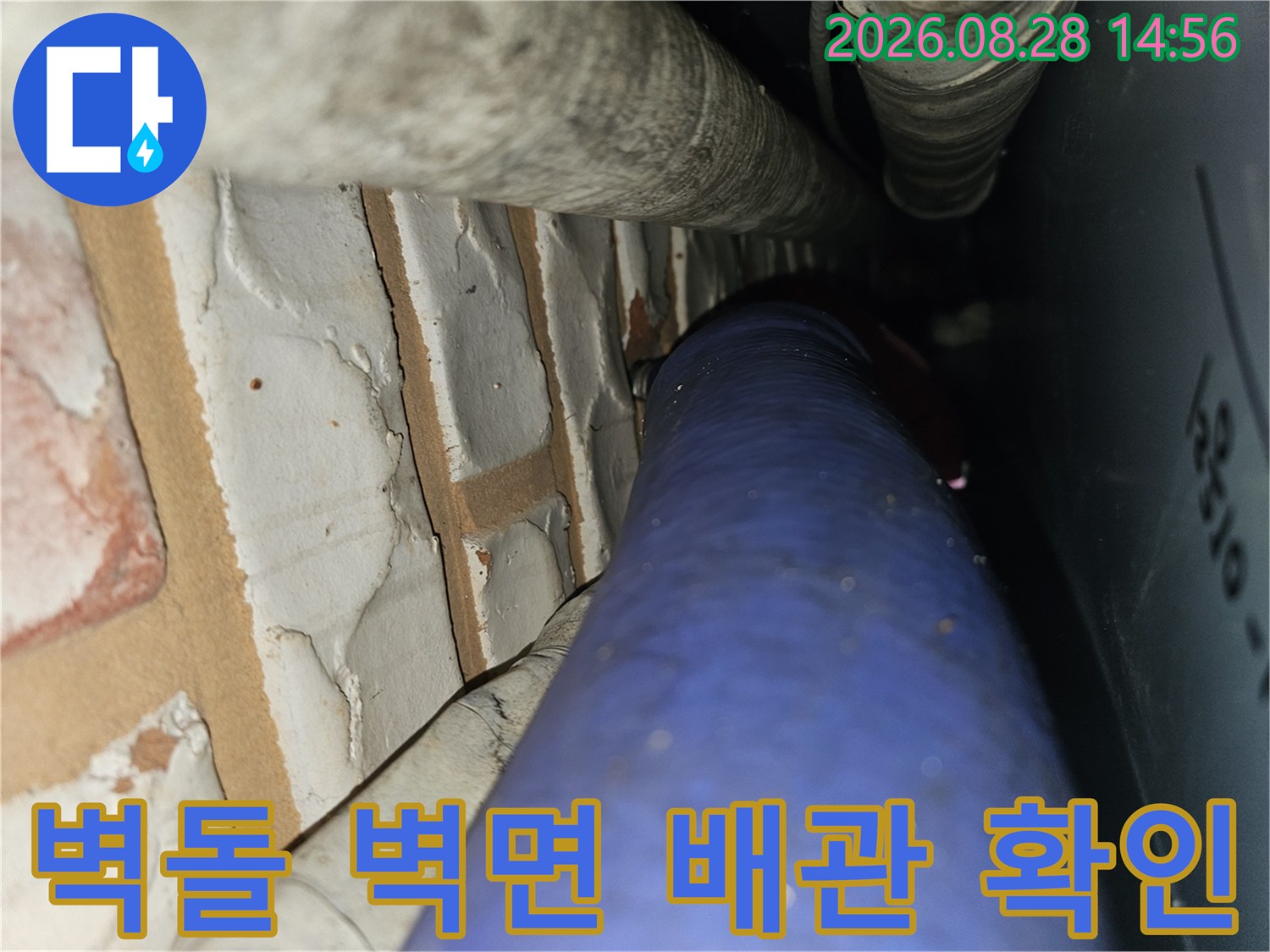 벽돌로 된 벽면 옆에 설치된 푸른색 수도 배관과 상단 연결 관로 모습입니다.