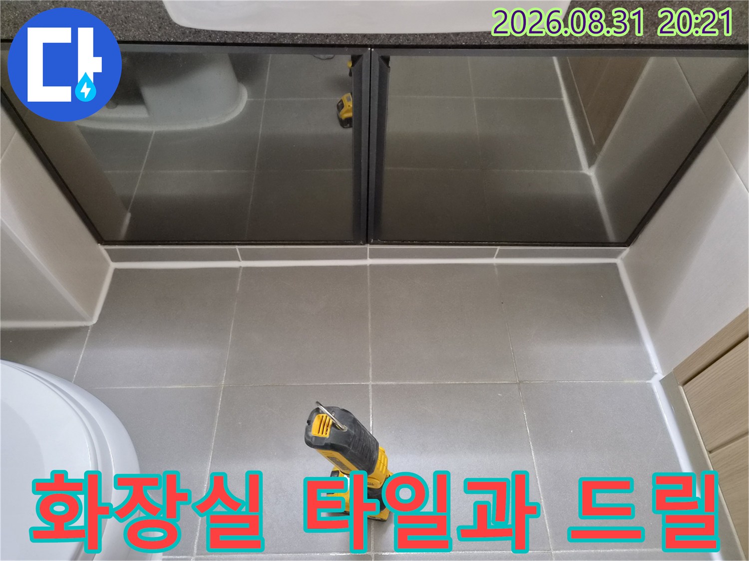 회색 타일 바닥에 놓인 전동 드릴과 세면대 밑 부분