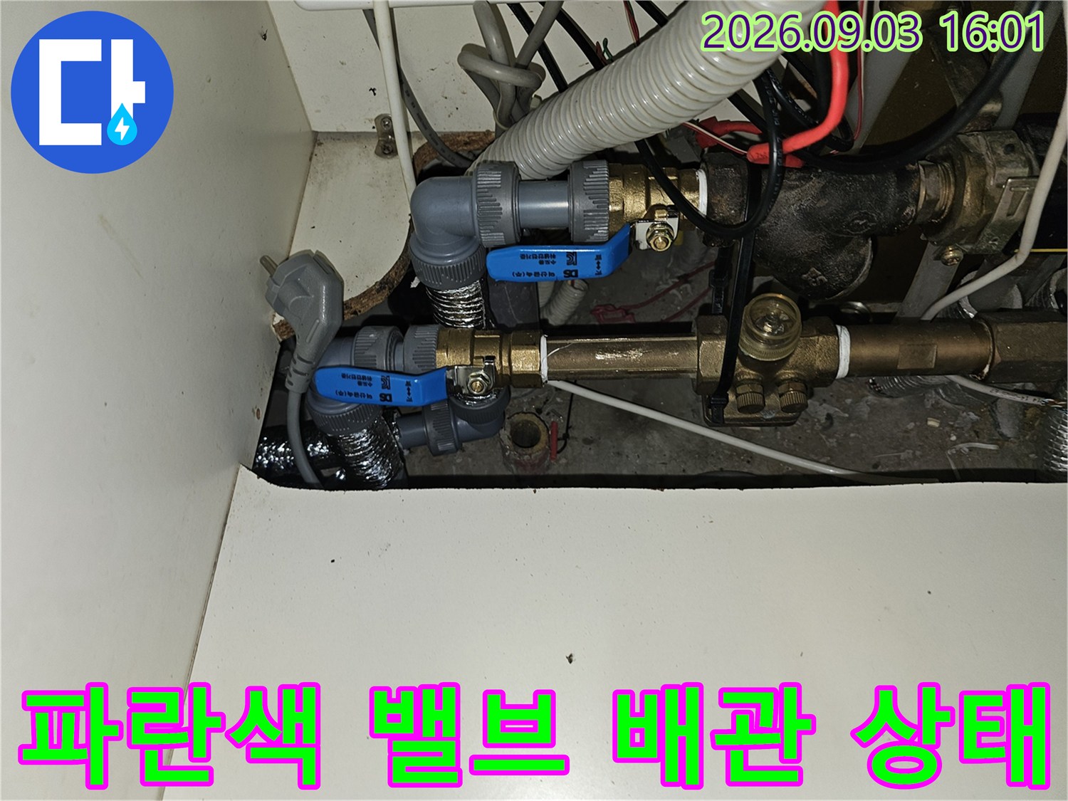 금속 배관과 파란색 핸들 밸브가 연결된 싱크대 하부입니다.
