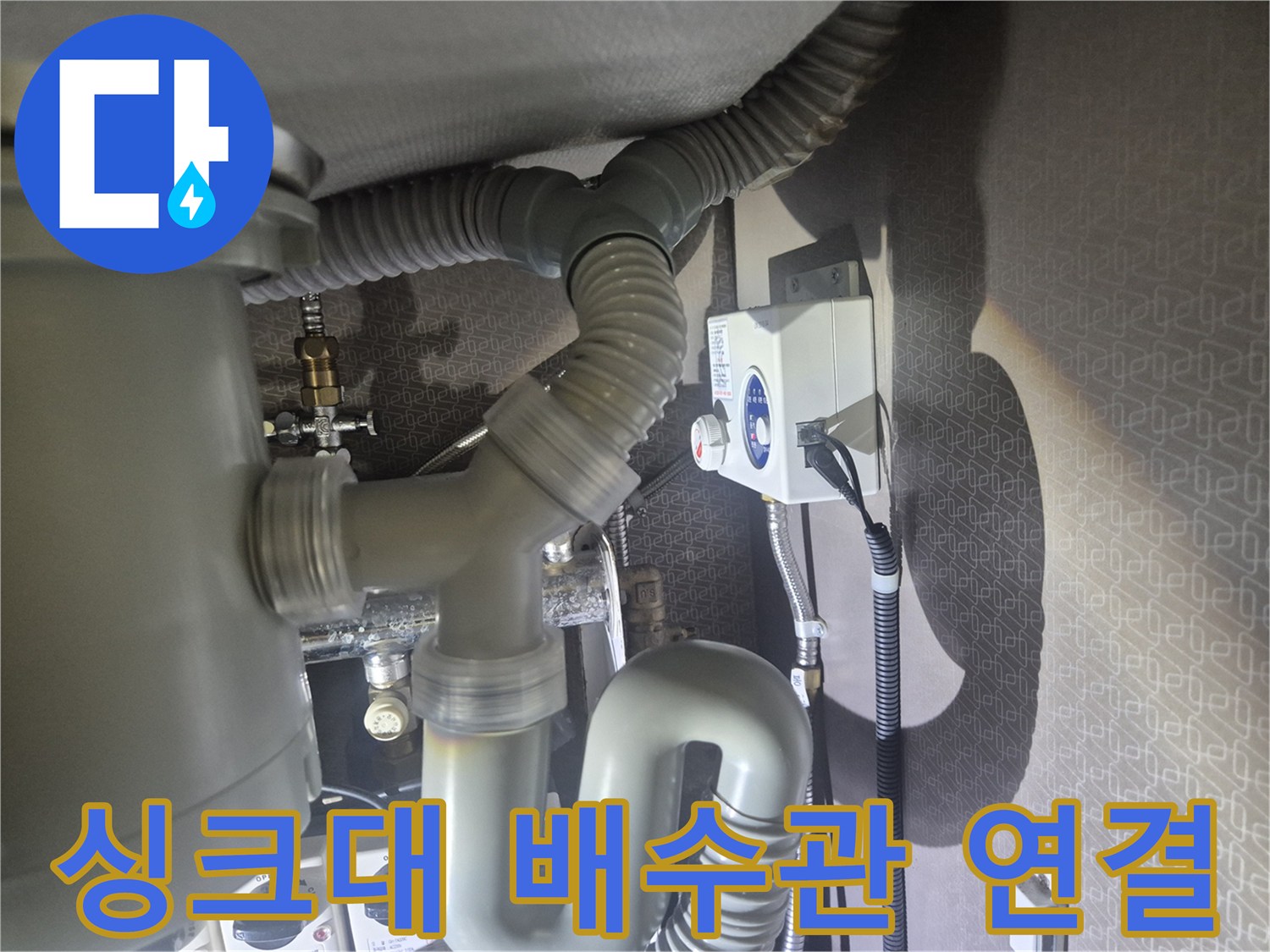 주방 싱크대 하부의 회색 자바라 호스와 배수 연결 부위 사진입니다.