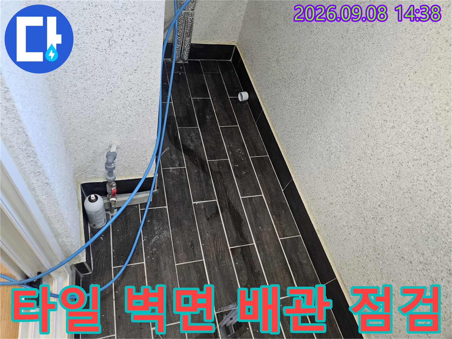 어두운 타일 사이로-파란색 호스가 연결된-배관 압력 측정 장비 모습입니다.