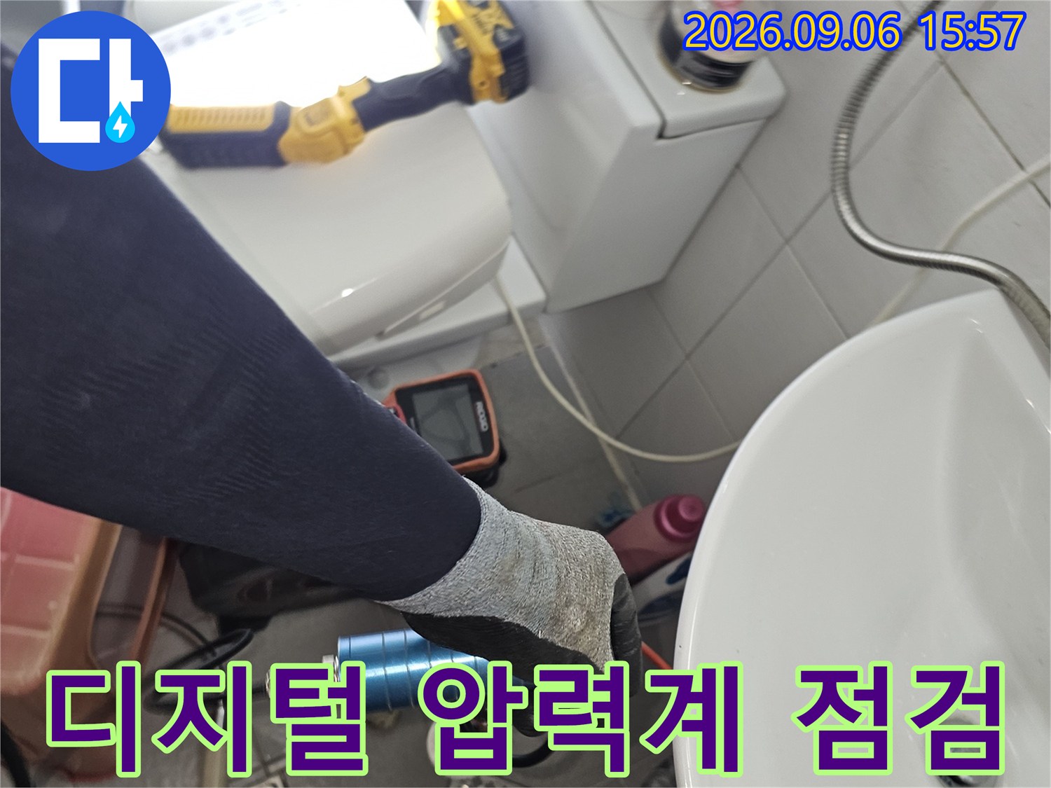화장실 바닥에서-디지털 압력계를 사용하여 배관의 기밀을 확인하는 모습입니다.
