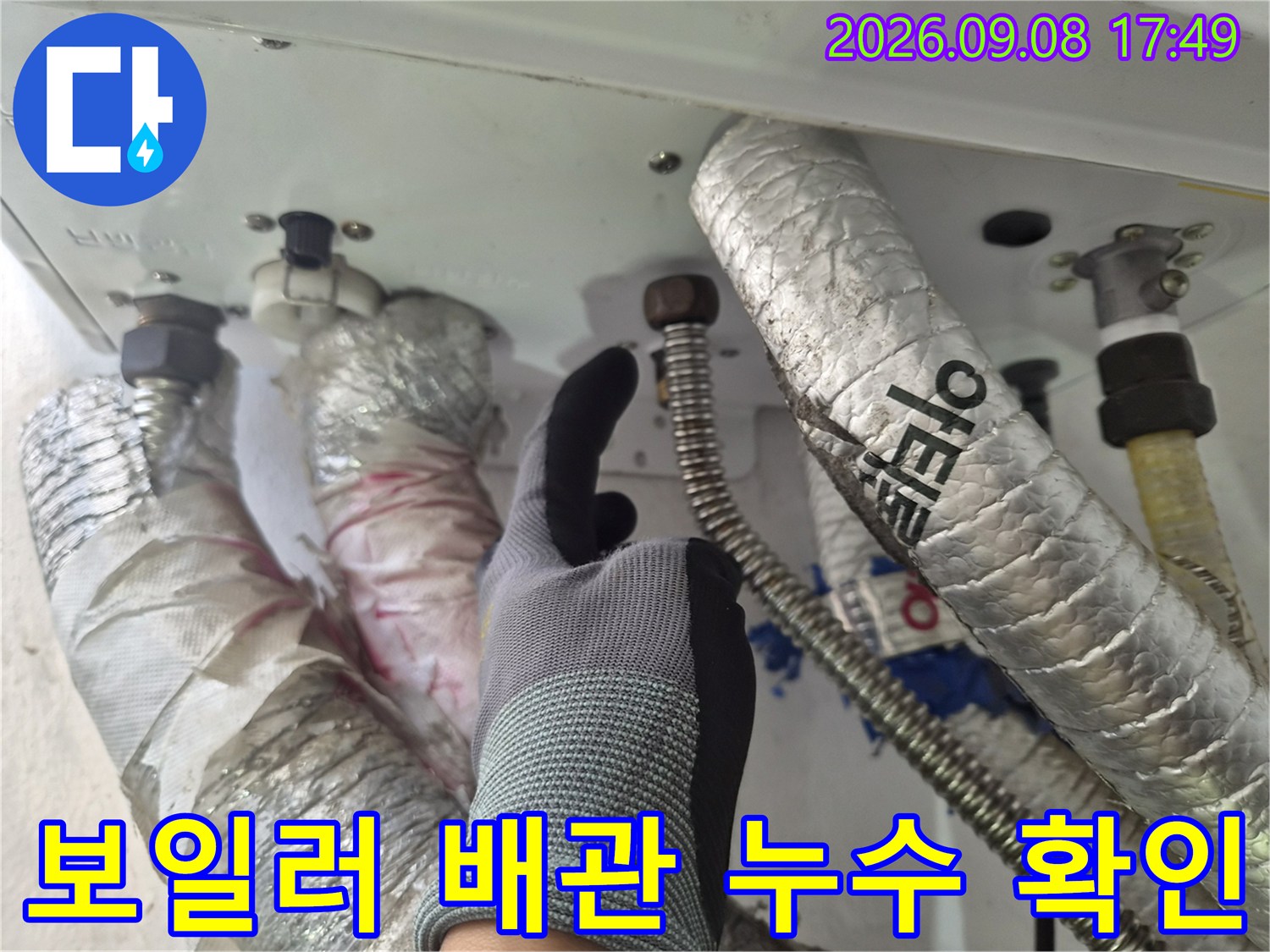 작업자가 보일러 하단 금속 연결 부위의 습기를 점검하는 사진입니다.