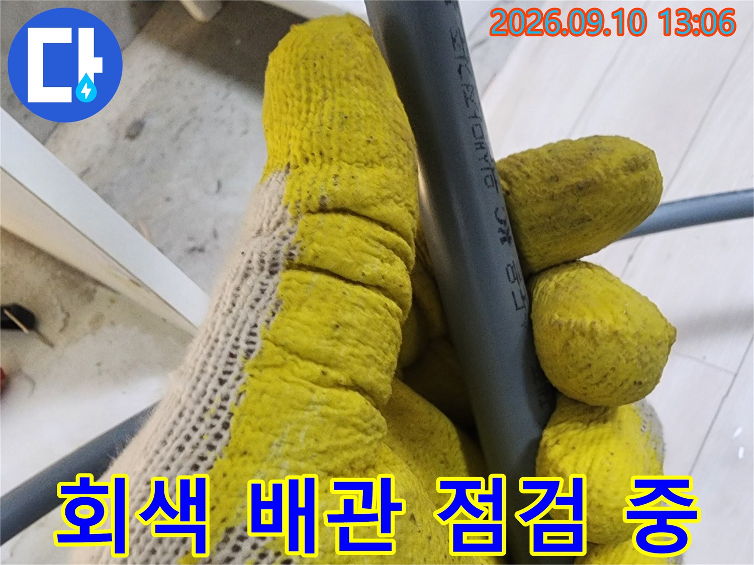 노란 장갑을 낀 손으로 회색 수도 배관의 표면을 면밀히 관찰하고 있습니다