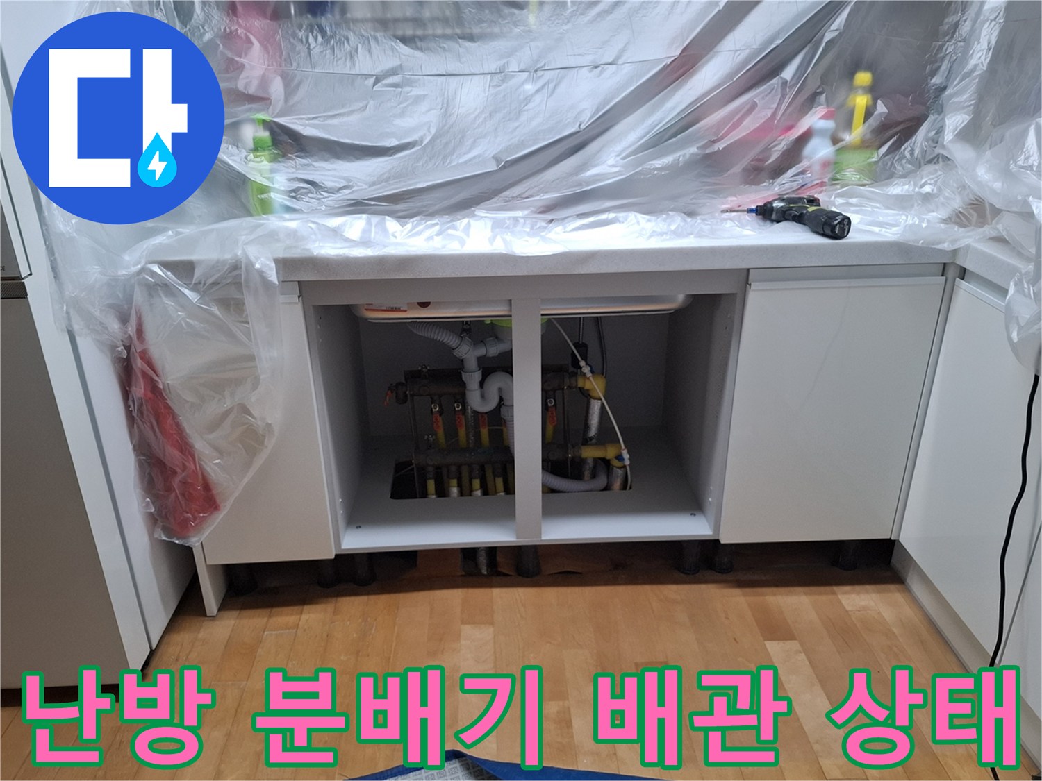 싱크대 아래쪽 난방 분배기의 연결 부위와 밸브를 촬영한 사진