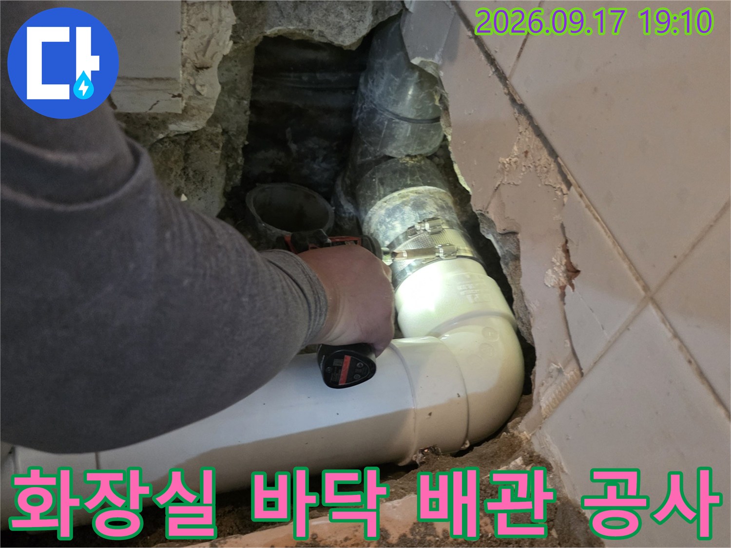 타일 아래 굴착된 공간에서 진행되는 PVC 배관 연결 및 교체 작업 장면입니다.
